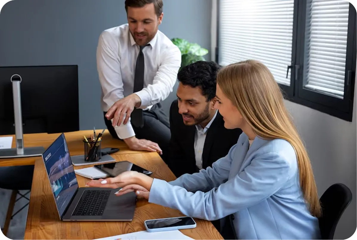 Team of professionals collaborating around a laptop in a modern office, reflecting skills built through Oratrics' best corporate training program